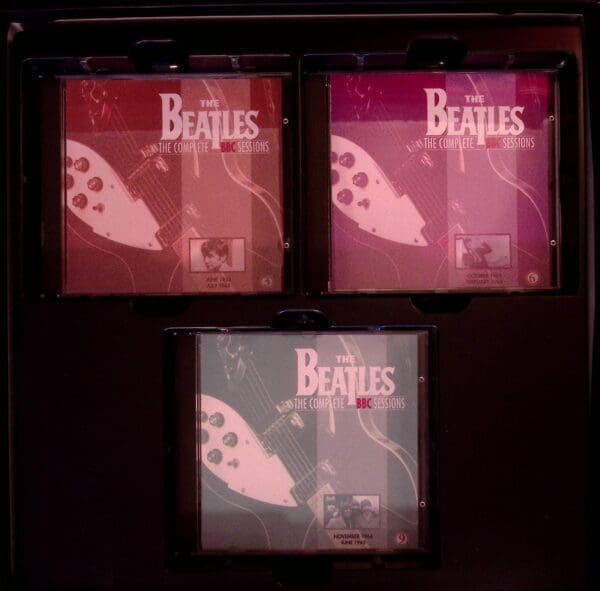 Three beatles cds are shown in a dark room.